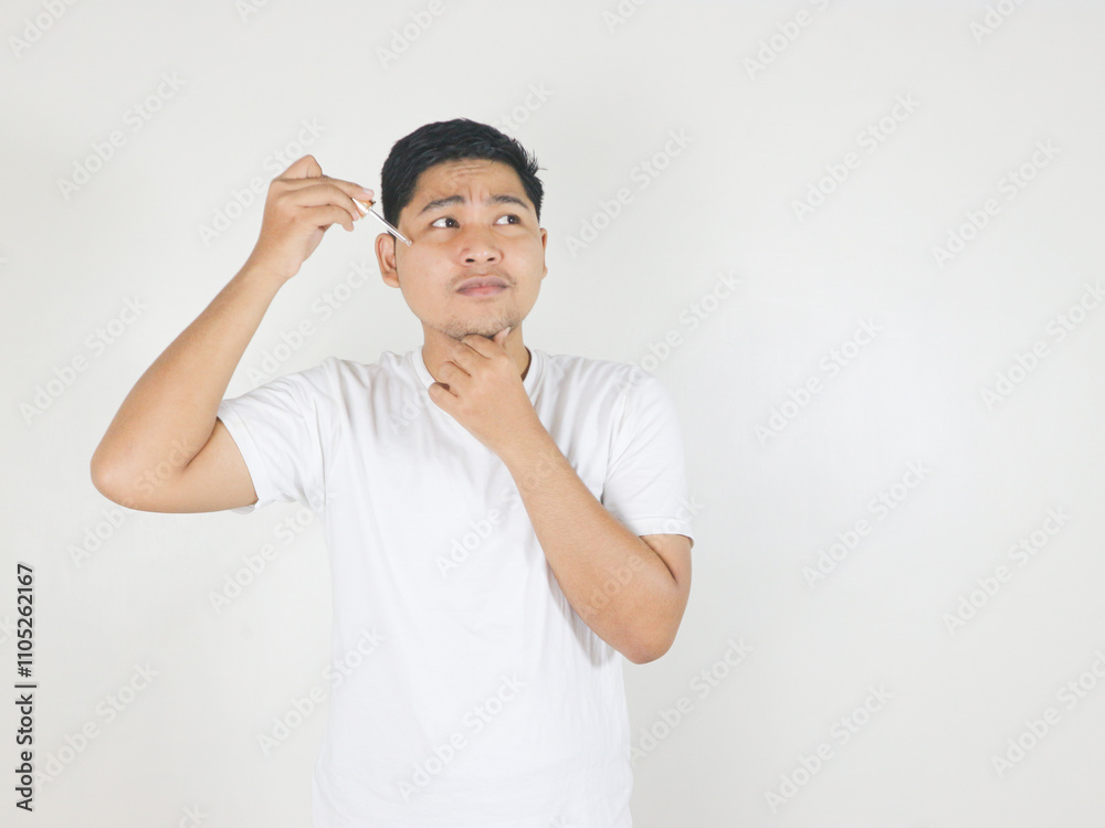 portrait of handsome guy applying serum beauty product on his face using glass pipette, with toughtfull face, and questioning gesture portrait of handsome guy applying serum beauty product on his face using glass pipette, with toughtfull face, and questioning gesture