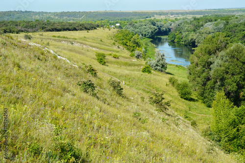 Foto Expansive grassy hills and a winding river with surrounding trees, showcasing a peaceful natural landscape under a clear sky