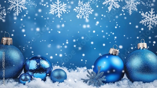 Winter scene with blue Christmas decorations. Shiny blue ornaments sit on simulated snow. Snowflakes fall against a vivid blue background. Festive winter theme.