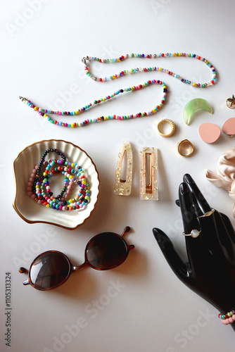 Obraz na płótnie Hand figurine, sunglasses, gold jewelry, colorful bead jewelry, statement rings and various hair accessories on the white table. Flat lay. w salonie