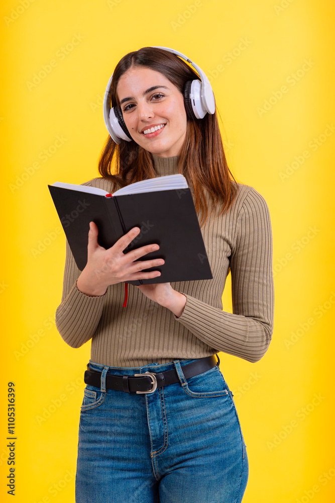 A cheerful young woman wearing white headphones and holding an open book, standing against a vibrant yellow background. Perfect image for learning, audiobooks, or educational themes.Vertical A cheerful young woman wearing white headphones and holding an open book, standing against a vibrant yellow background. Perfect image for learning, audiobooks, or educational themes.Vertical