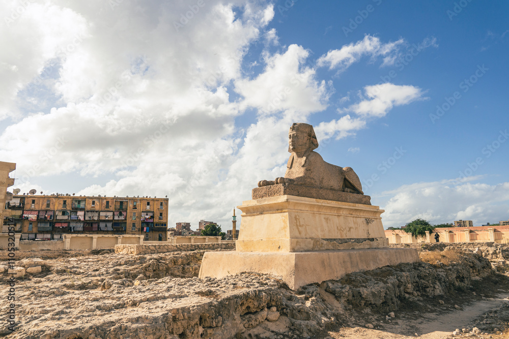 Φωτογραφία Statue of the ancient Sphinx on background of modern houses and blue cloudy sky