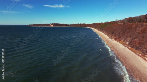 An aerial view of a long beach with a peninsula in Stony Brook on Long Island, NY on a sunny day with blue skies and white clouds. The drone camera dolly in and boom up to reveal the horizon. photo