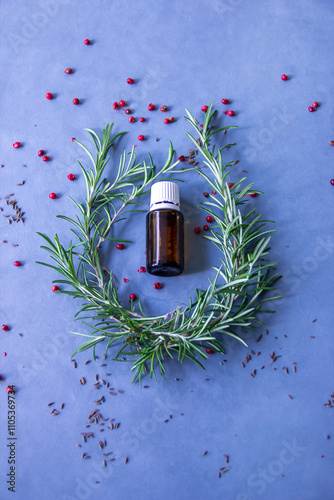 Essential oil bottle surrounded by aromatic herbs and spices on a blue background