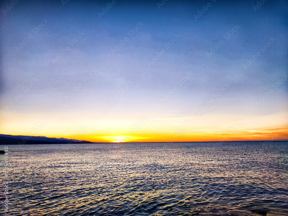 Naklejka premium Sunset over the tranquil ocean at a coastal location with soft colors painting the sky and water in the early evening