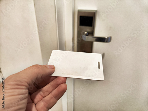 A hand holding a blank keycard near a hotel door lock in a well-lit corridor during daytime photo