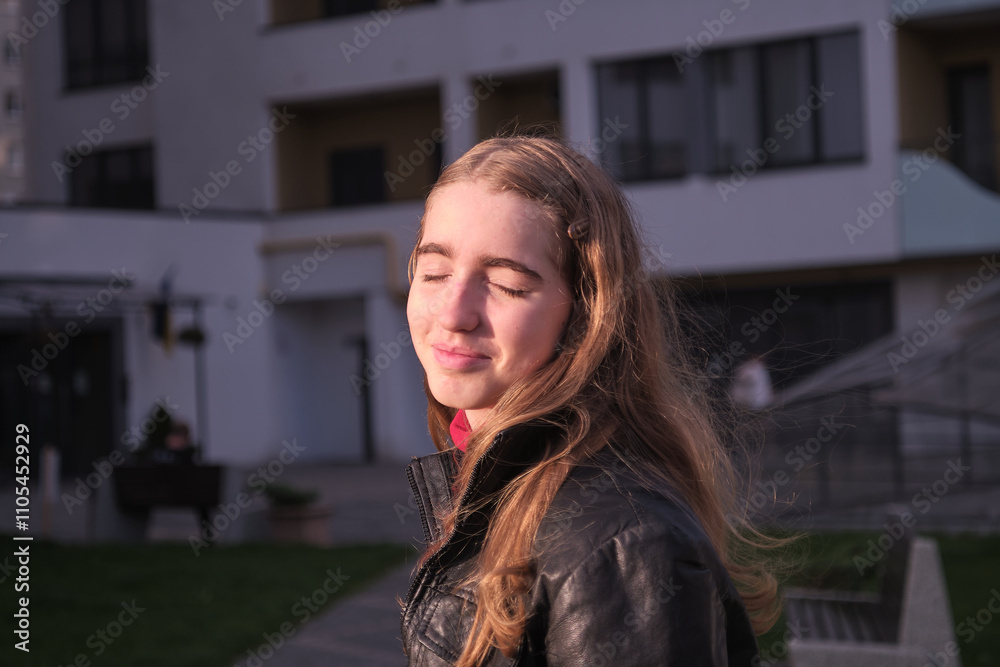 cheerful caucasian girl with closed eyes enjoying warm sunlight outdoors, wearing a leather jacket, with urban architecture in the background. A moment of relaxation and happiness. cheerful caucasian girl with closed eyes enjoying warm sunlight outdoors, wearing a leather jacket, with urban architecture in the background. A moment of relaxation and happiness.