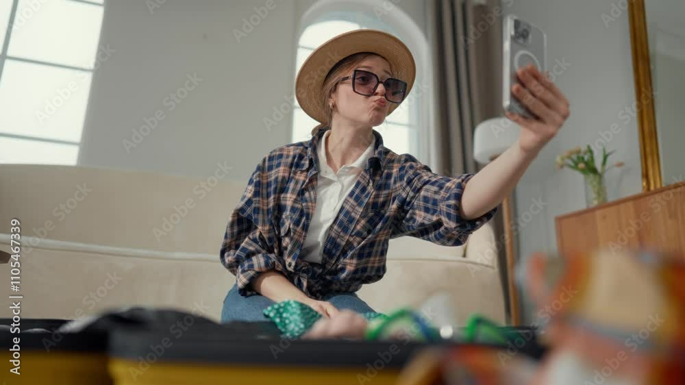 Funny girl with sunglasses and straw hat taking selfie when packing suitcase. Preparing to trip in summer weekend, joyful woman smiling to camera, making content for social media, happiness and joy Funny girl with sunglasses and straw hat taking selfie when packing suitcase. Preparing to trip in summer weekend, joyful woman smiling to camera, making content for social media, happiness and joy
