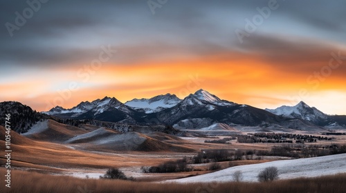 Scenic winter landscape with snow-capped mountains and rolling hills under a dramatic sunset sky featuring vibrant orange and blue hues.