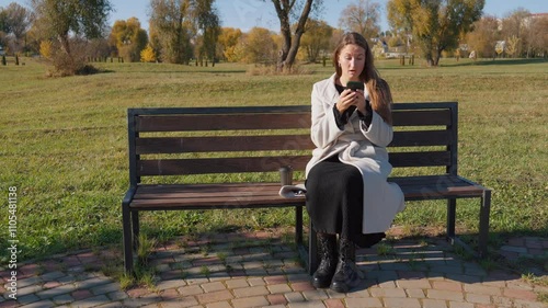 Young woman sitting on park bench, looking shocked while reading text message on her smartphone. Concern and worry are evident as she processes bad news