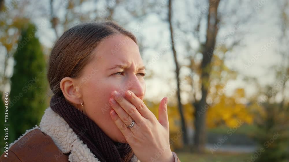 sleepy woman sitting on bench in autumn park, yawning; yawning facial expression from sleepless night, fatigue, insomnia, insufficient sleep, exhaustion, stress, fatigue