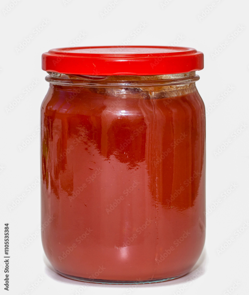 A jar of red sauce is sitting on a white background A jar of red sauce is sitting on a white background