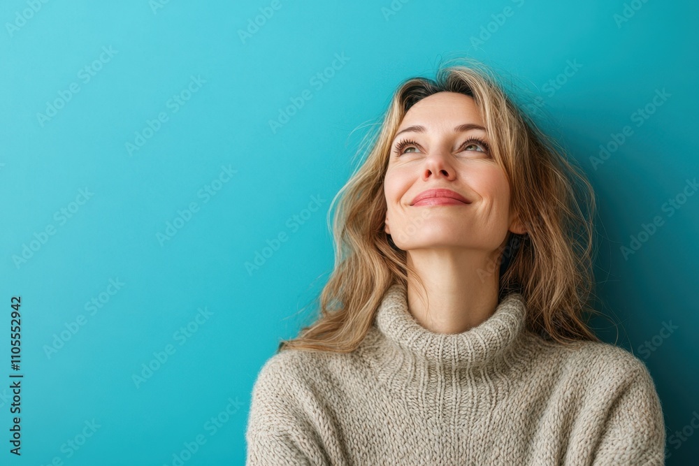 Woman smiles while looking up against a bright blue wall in soft sweater Woman smiles while looking up against a bright blue wall in soft sweater