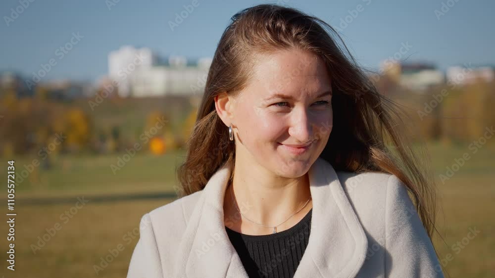 Businesswoman smiles outdoors on sunny autumn day, with her hair blowing in wind. Vibrant colors of fall create cheerful backdrop for her confident expression Businesswoman smiles outdoors on sunny autumn day, with her hair blowing in wind. Vibrant colors of fall create cheerful backdrop for her confident expression