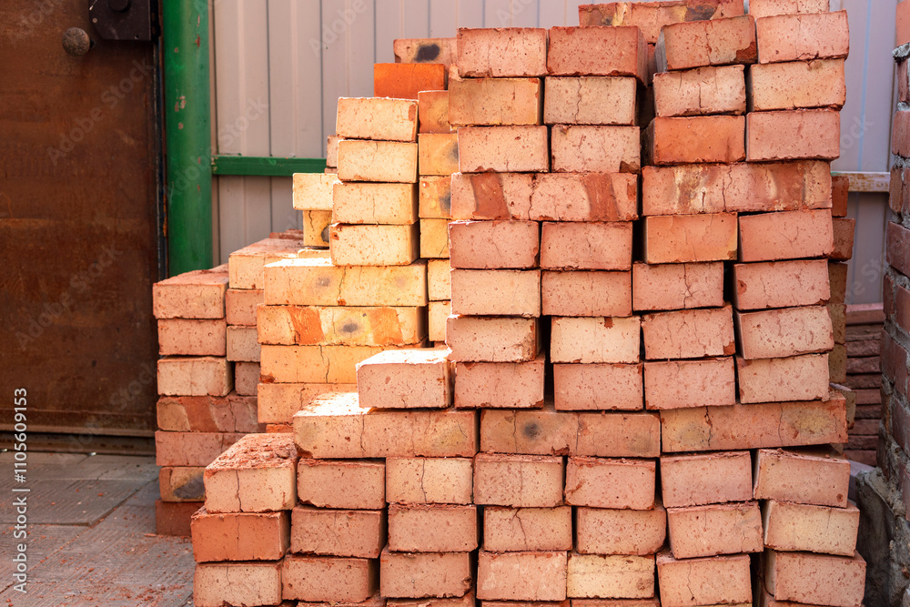 Fototapeta premium Stack of red bricks on concrete foundation, process of house building. Concrete foundation with bricks for laying. Building materials at construction
