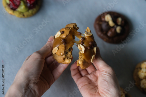 Fotografi Woman breaks homemade american traditional chocolate chip cookie with peanut butter, gooey caramel and peanuts topping
