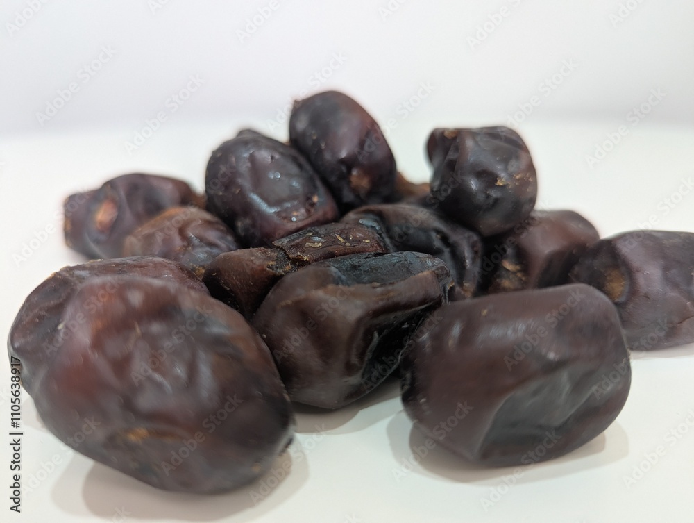 Close-up of fresh dates arranged on a white table, emphasizing their natural texture and rich brown hue. The photo highlights the glossy, plump fruits, renowned for their sweet taste \