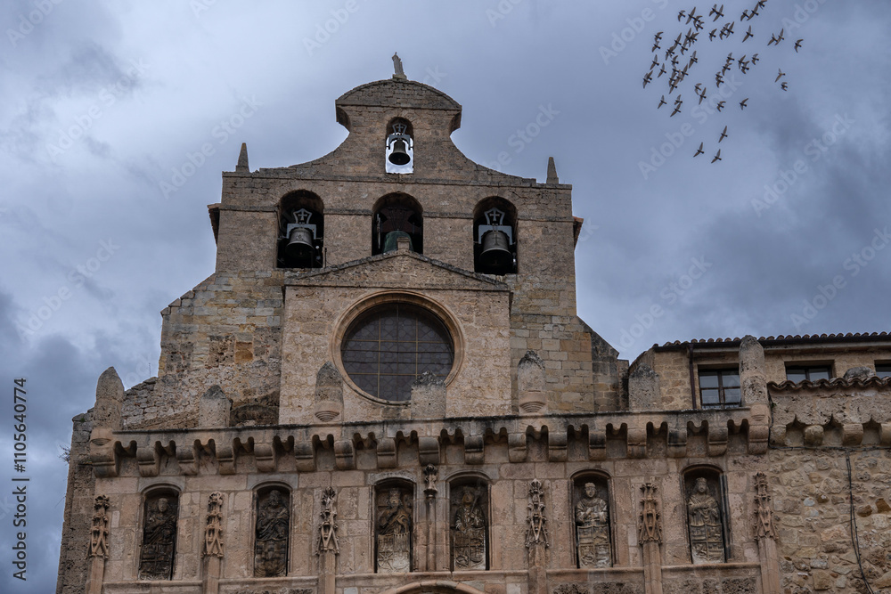 Fototapeta premium Monastery of San Salvador front facade in a stormy day with a bird flock on the sky. Oña village in Spain