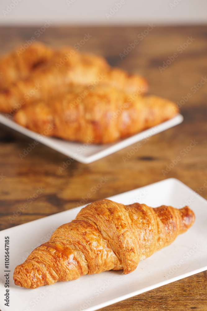 Artisan croissant handmade in a bakery. Close-up of croissant on a rectangular white plate. Continental breakfast, to be filled with sweet or savory ingredients. Artisan croissant handmade in a bakery. Close-up of croissant on a rectangular white plate. Continental breakfast, to be filled with sweet or savory ingredients.