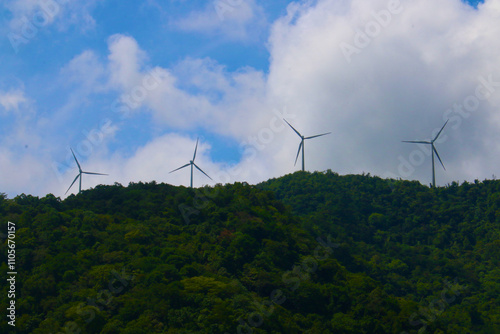 Windmills on top of a mountain. Four windmills on top of a jungle-covered mountain range against a sky of clouds.