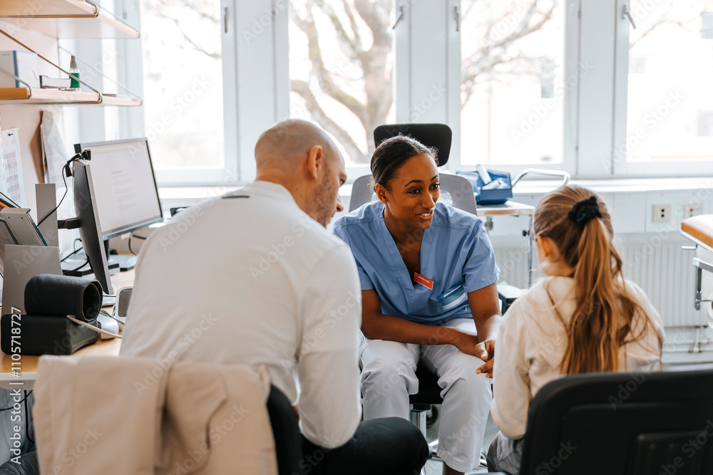 Happy female pediatrician discussing with girl sitting next to father in examination room at hospital Happy female pediatrician discussing with girl sitting next to father in examination room at hospital