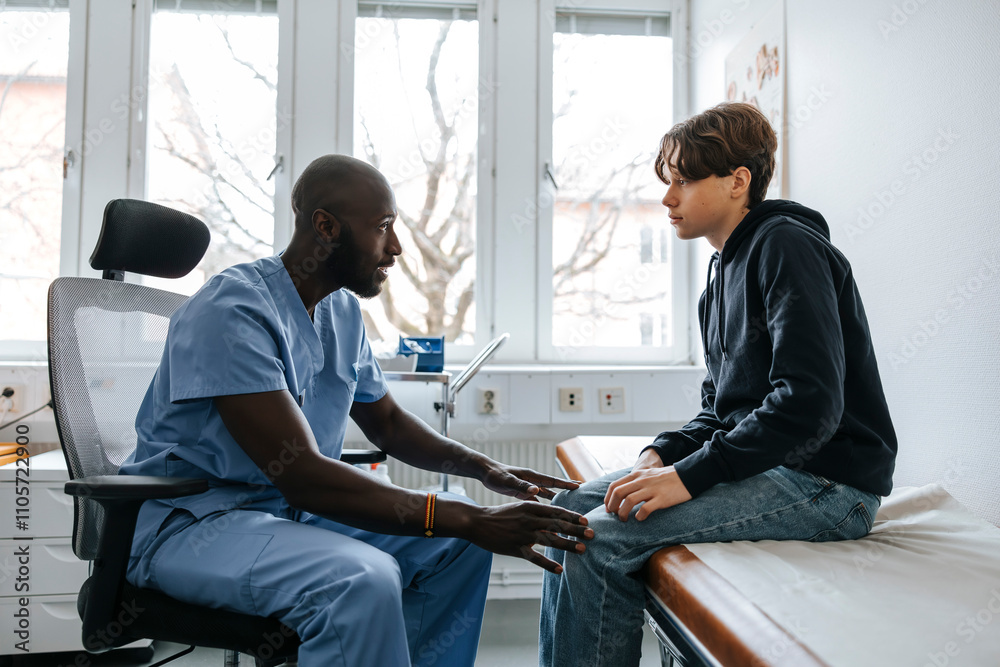 Male medical professional consoling teenage patient sitting on bed in examination room