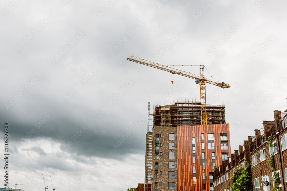 Fototapeta premium Construction crane and modern building under cloudy sky