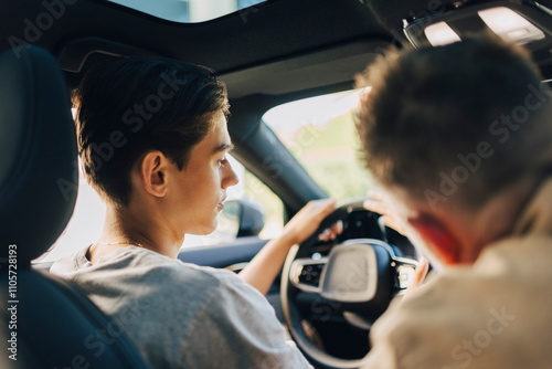 Father giving driving lessons to son while sitting in car photo