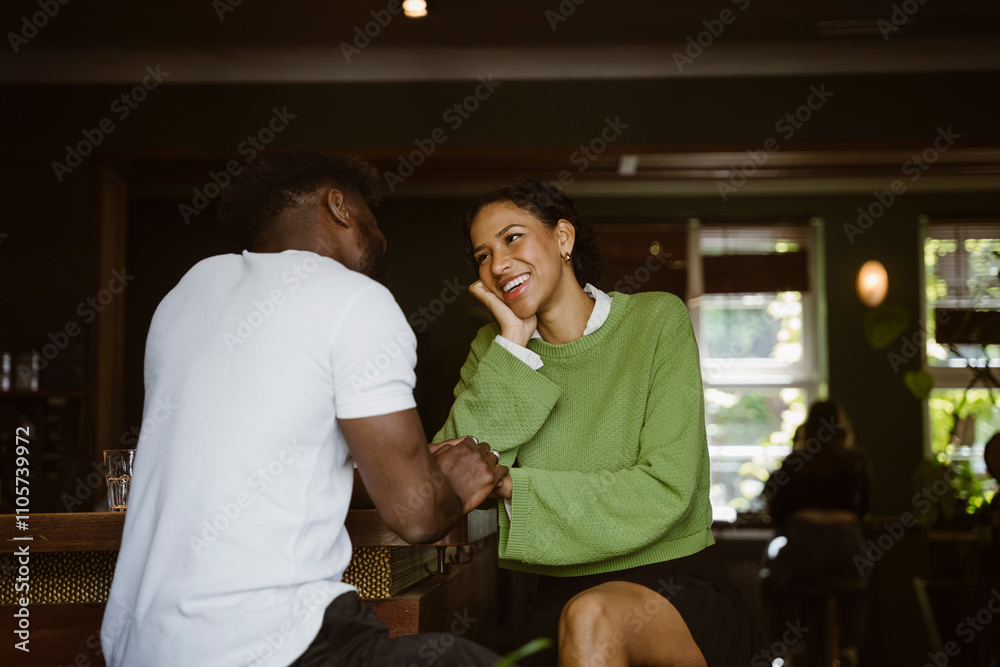 Smiling woman leaning on elbow and glancing at boyfriend sitting in bar Smiling woman leaning on elbow and glancing at boyfriend sitting in bar