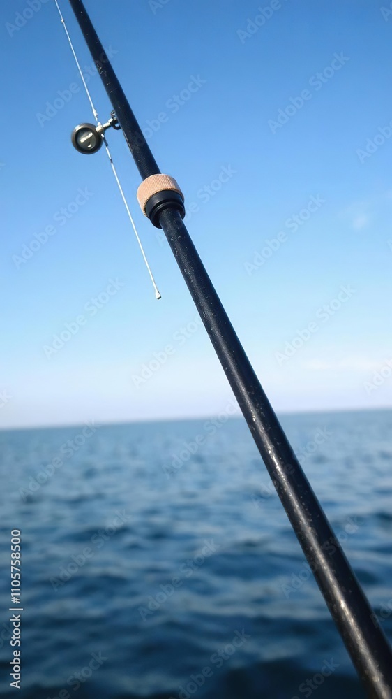 Fototapeta premium A sleek and stylish fishing rod set against a serene blue background, perfect for any angler looking to catch some big fish, fishing hobby, recreational activity, fishing pole