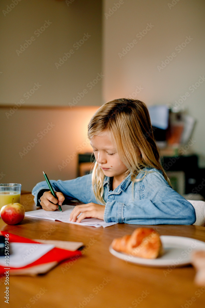 Focused boy with blond long hair writing on book while dong homework at home Focused boy with blond long hair writing on book while dong homework at home