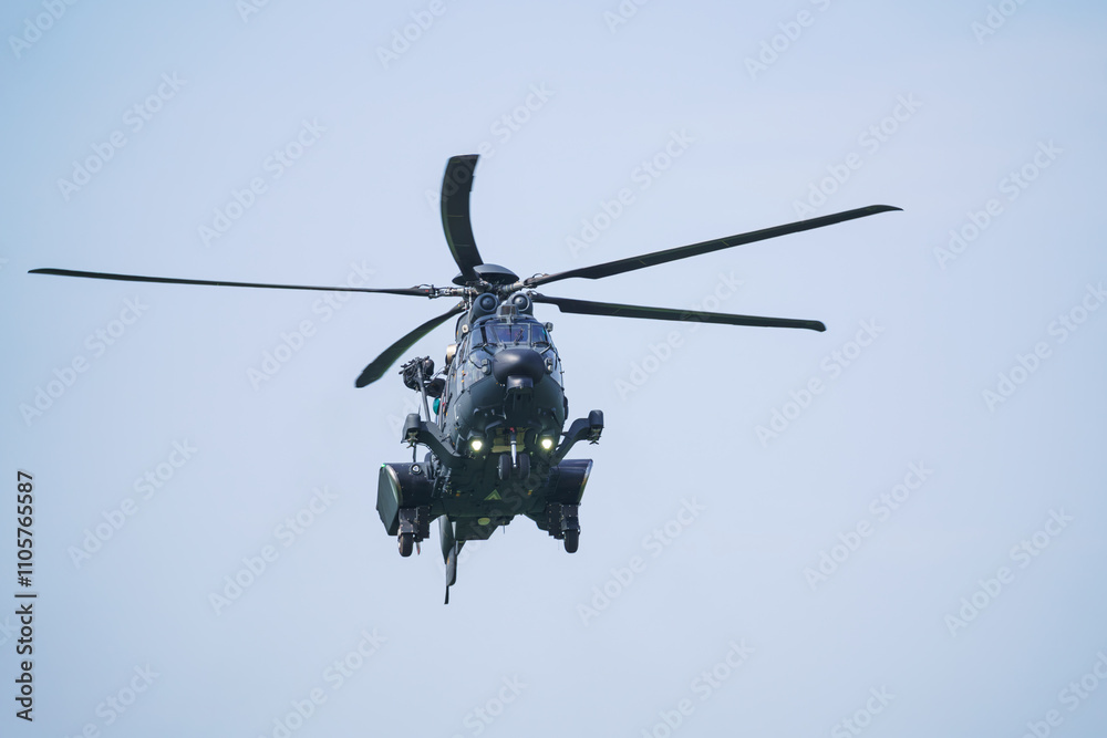 Fototapeta premium The military helicopter is hovering in the air, facing forward at an airshow. Blue background.
