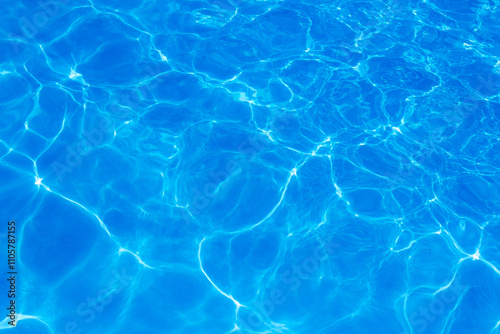 Clear blue swimming pool water surface with sunlight reflections creating abstract patterns and ripples, evoking a refreshing and tranquil summer vibe.