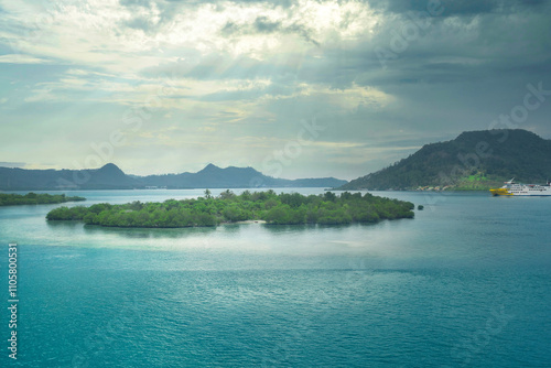 A body of teal water with islands, lush green vegetation, and a ship in the distance. Cloudy sky. photo