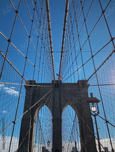 A sunny day walk across the iconic Brooklyn Bridge in New York City, showcasing its intricate suspension cables and stunning architectural details against a clear blue sky