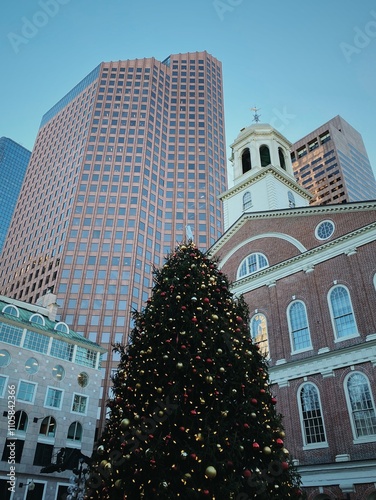 Festive holiday spirit in downtown Boston – A beautifully adorned Christmas tree stands in front of the historic Faneuil Hall, surrounded by modern skyscrapers, blending tradition and contemporary urb