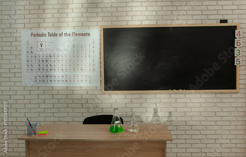 Empty elementary school chemistry classroom with chalkboard, workspace for studying. Shot of teacher's desk with glass bottle, periodic table on the wall.