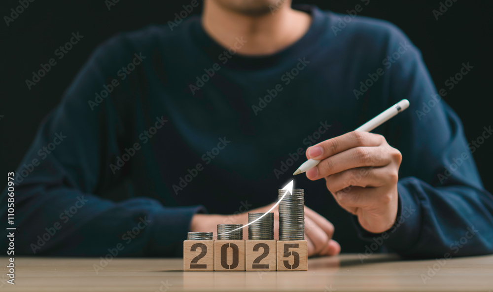 a person uses a pen to point stacked coins on wooden blocks upcoming new year 2025, financial growth, investment planning, new business beginnings, financial growth, and strategic planning and goals