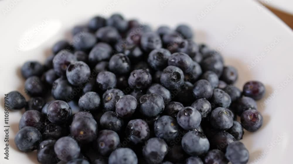 White plate is rotating, presenting a mound of freshly washed blueberries. The blueberries are piled high on the plate, and the camera is focused on the fruit White plate is rotating, presenting a mound of freshly washed blueberries. The blueberries are piled high on the plate, and the camera is focused on the fruit
