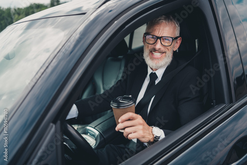 Confident senior businessman wearing a formal suit, enjoying coffee in his car parked on a city street