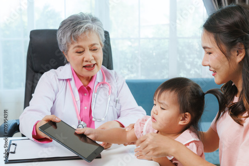 Happy senior female pediatrician professional doctor talk and play to asian girl sitting on mother before exam treatment at hospital or clinic. asia medical child health care.