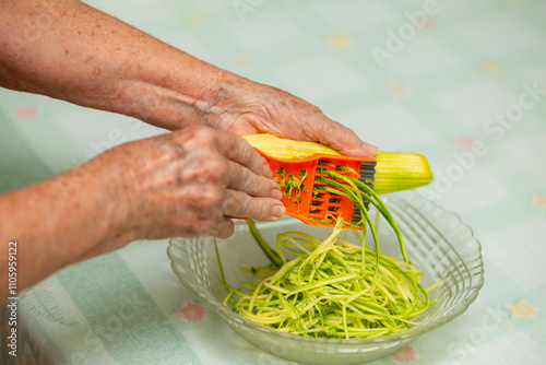 Mãos de uma cozinheira ralando uma abobrinha para uma vasilha de vidro. photo