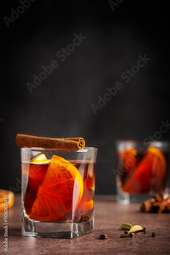Homemade traditional winter red mulled wine drink or grog cocktail made with slices of orange citrus fruit decorated with cinnamon stick served in glass on brown table on black wall with copy space