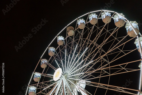 giant illuminated ferris wheel with white cabins glowing against the dark night sky, festive attraction, modern design, and dramatic perspective photo