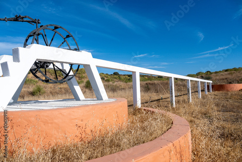 Historical water well with white metal frame and black wheel photo