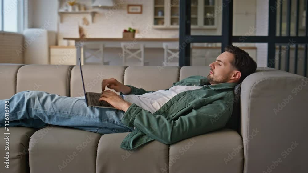 Man working laptop lying comfortable at home couch. Busy guy freelancer work