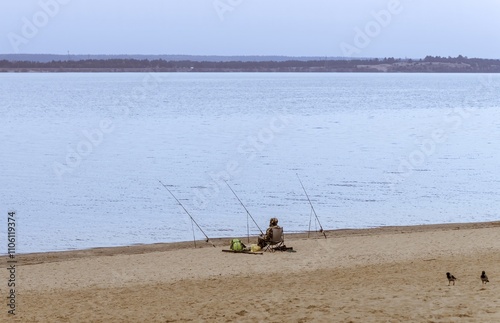 A sitting fisherman with fishing rods on the background of a river landscape