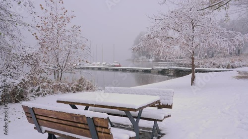 public benches covered in snow during a snowfall on the lakeside