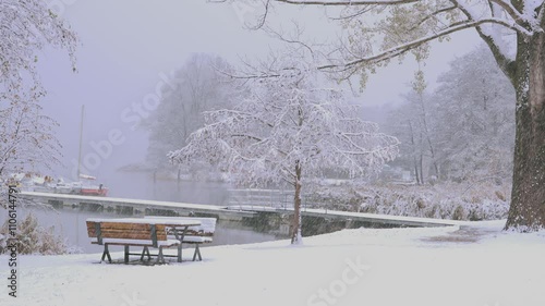 public benches covered in snow during a snowfall on the lakeside