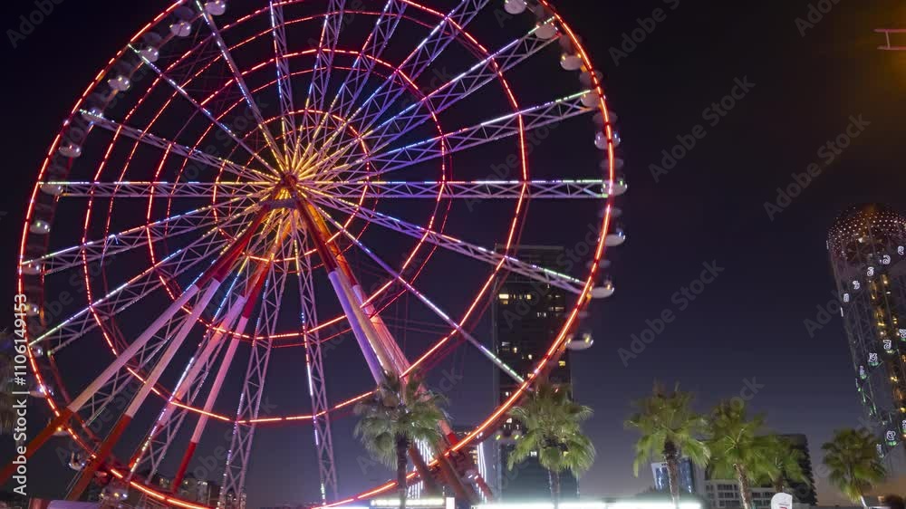 Timelapse of moving illuminated Ferris wheel on embankment in Batumi evening.